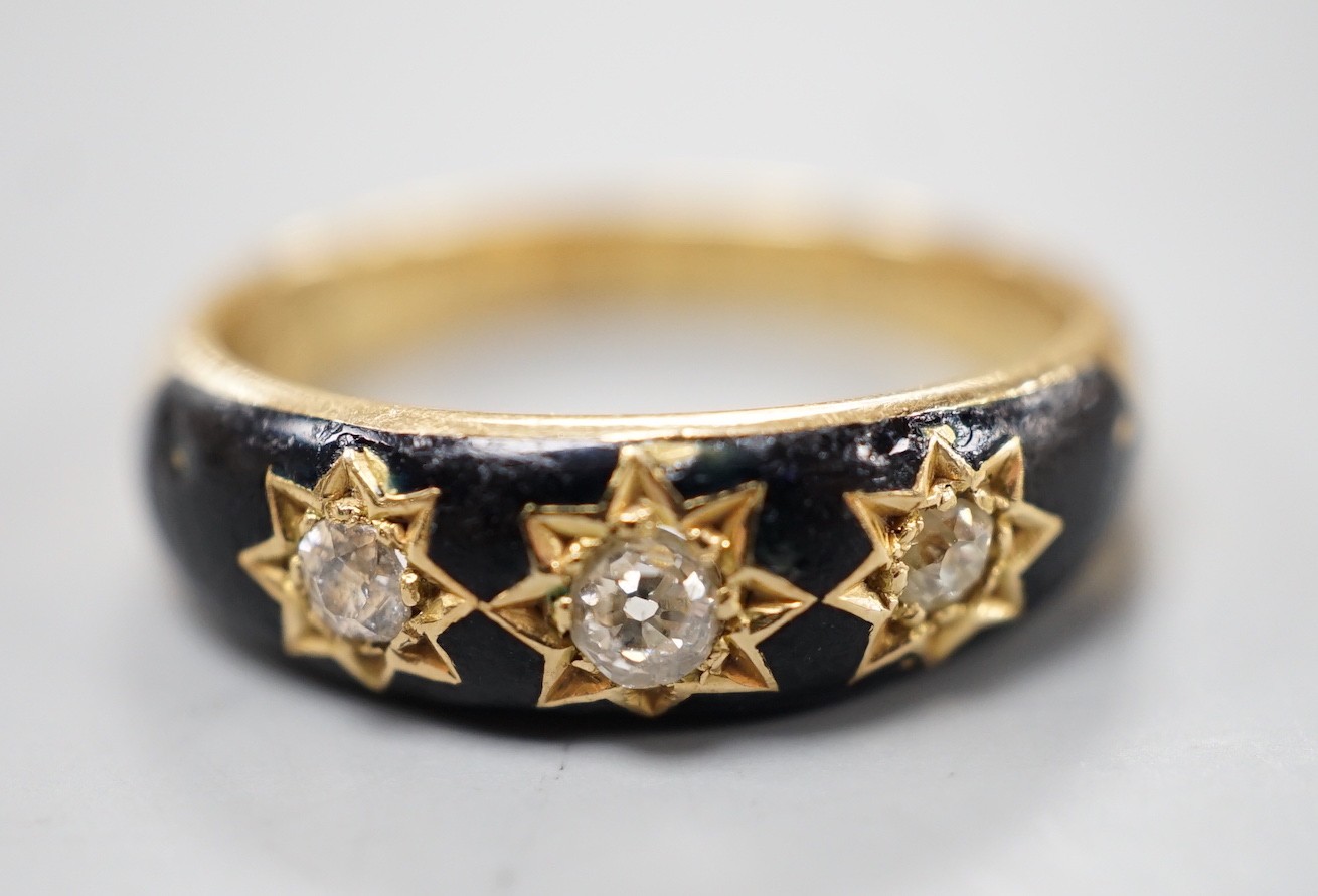 An Edwardian 18ct, black enamel and three stone gypsy set diamond mourning ring, size Q/R, gross weight 6.6. grams, the interior shank inscribed 'Sacred to the memory of my beloved husband'.